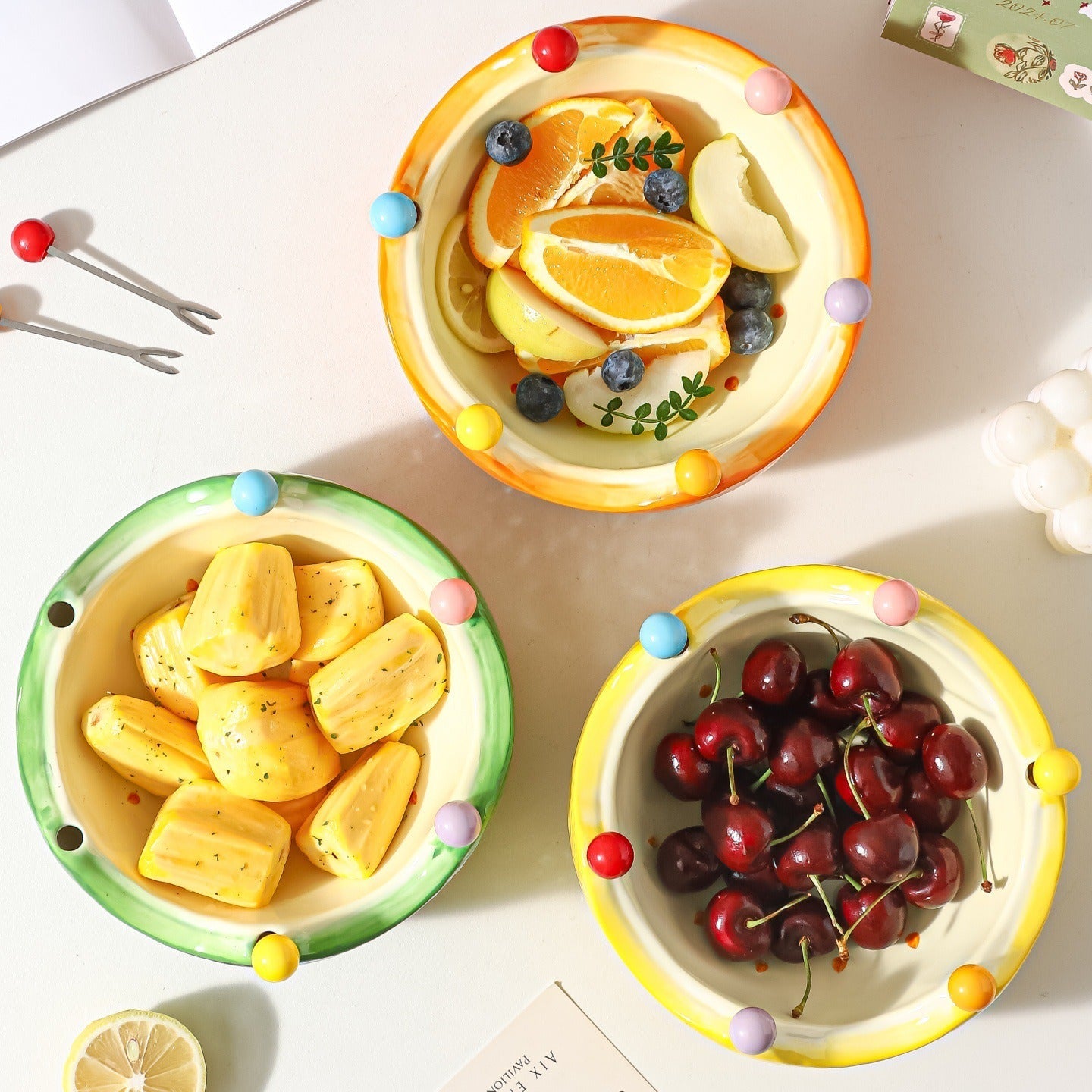 Overhead view of colorful ceramic crown fruit bowls serving orange slices crackers and cherries