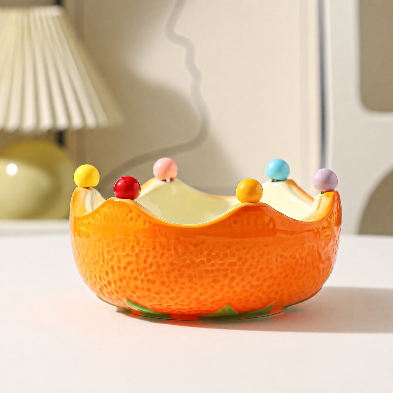 Orange ceramic crown fruit bowl with glossy finish and colorful bead accents on a tabletop