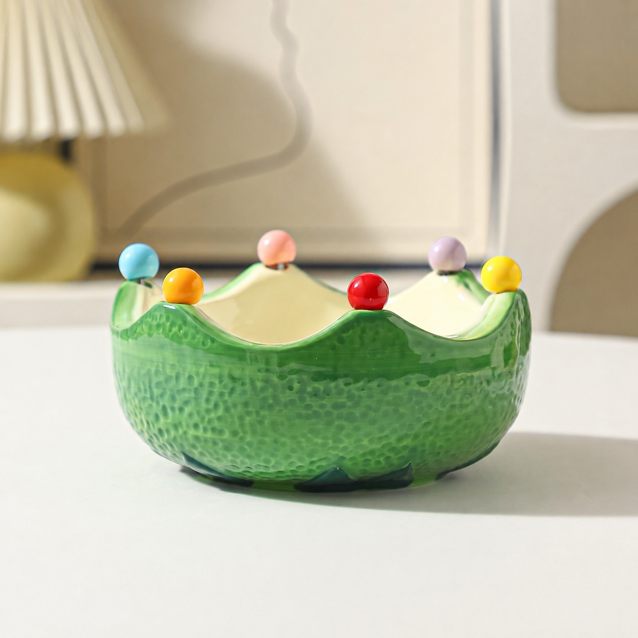 Green ceramic crown fruit bowl with glossy finish and colorful bead accents on a tabletop
