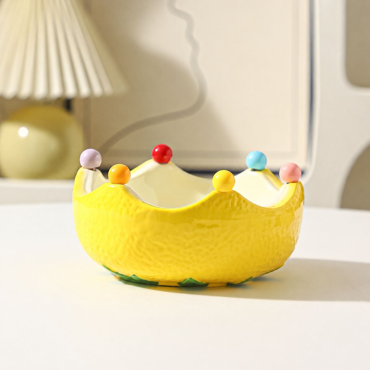 Yellow ceramic crown fruit bowl with glossy finish and colorful bead accents on a tabletop