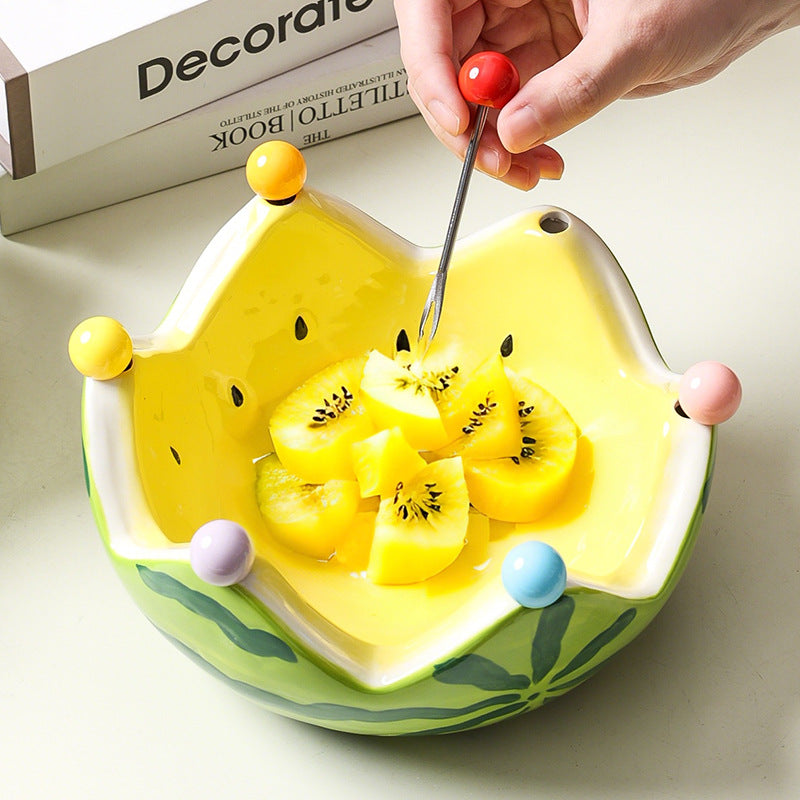 Yellow ceramic crown fruit bowl holding sliced fruit with a hand using a fruit fork