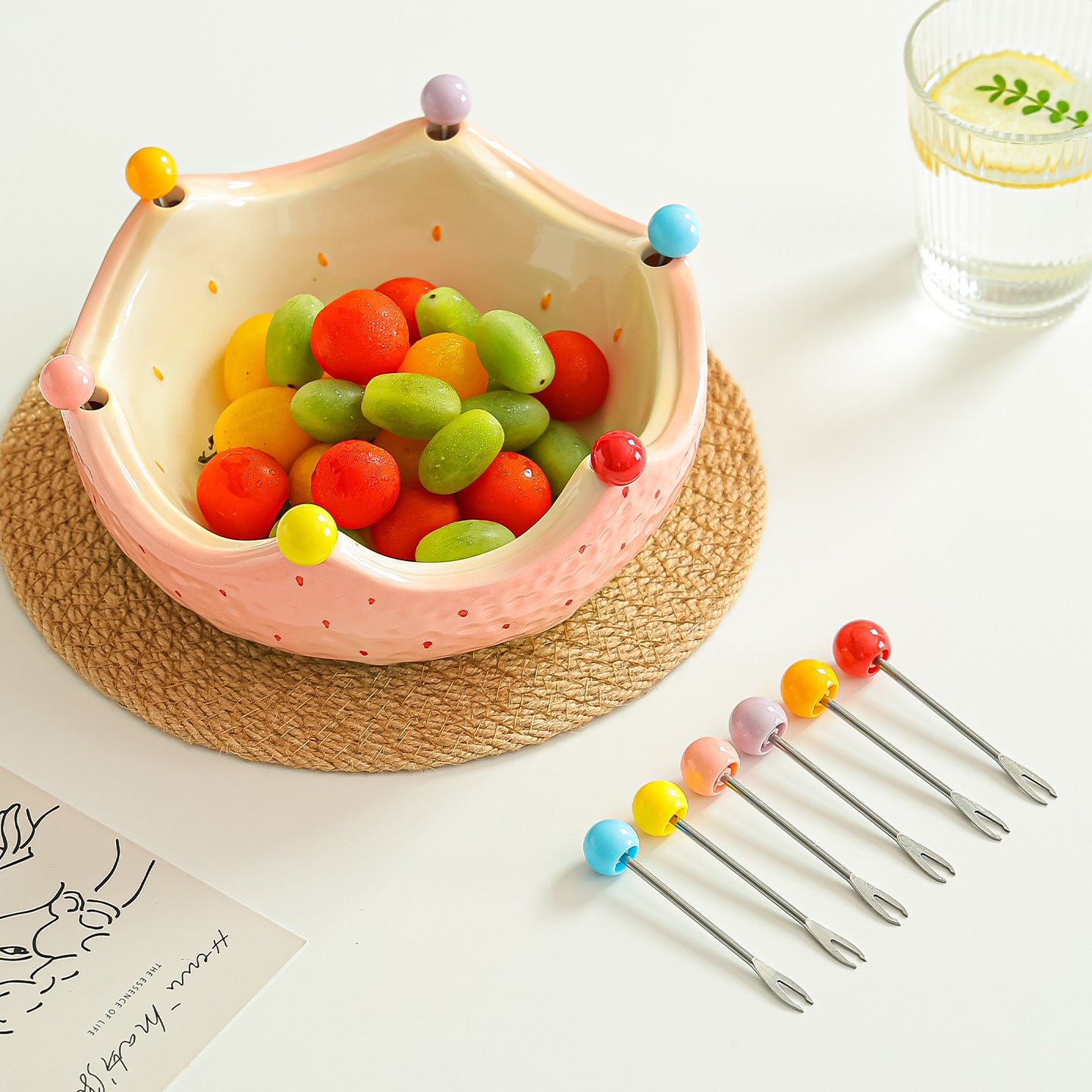 Pink ceramic crown fruit bowl filled with fruit with six matching fruit forks beside it