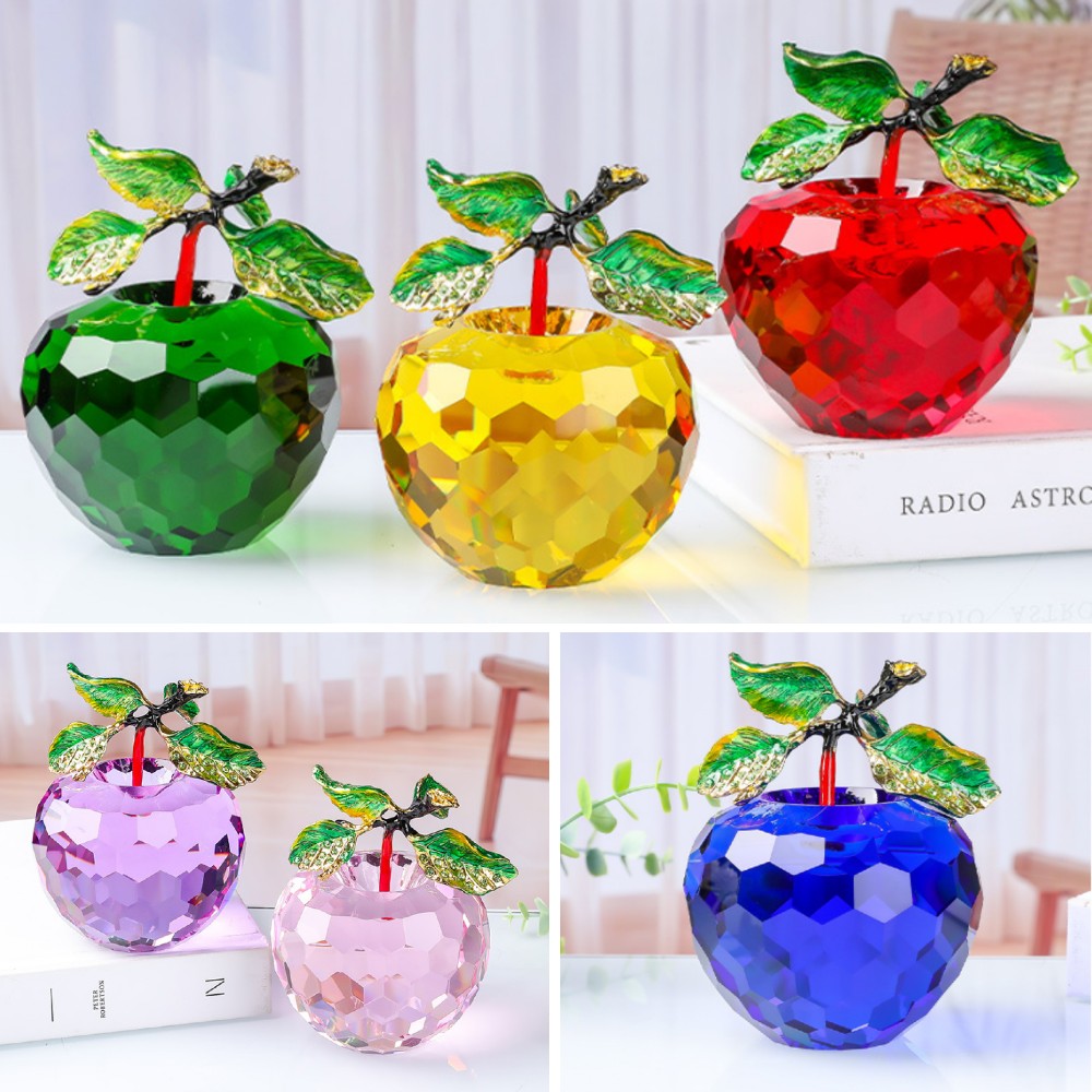 Colorful crystal apples with green leaves on a white surface