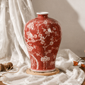 Red plum blossom ceramic vase styled with soft fabric and decorative accents