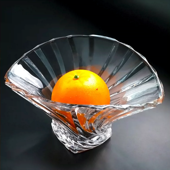 Clear flared glass centerpiece bowl holding an orange against a dark background
