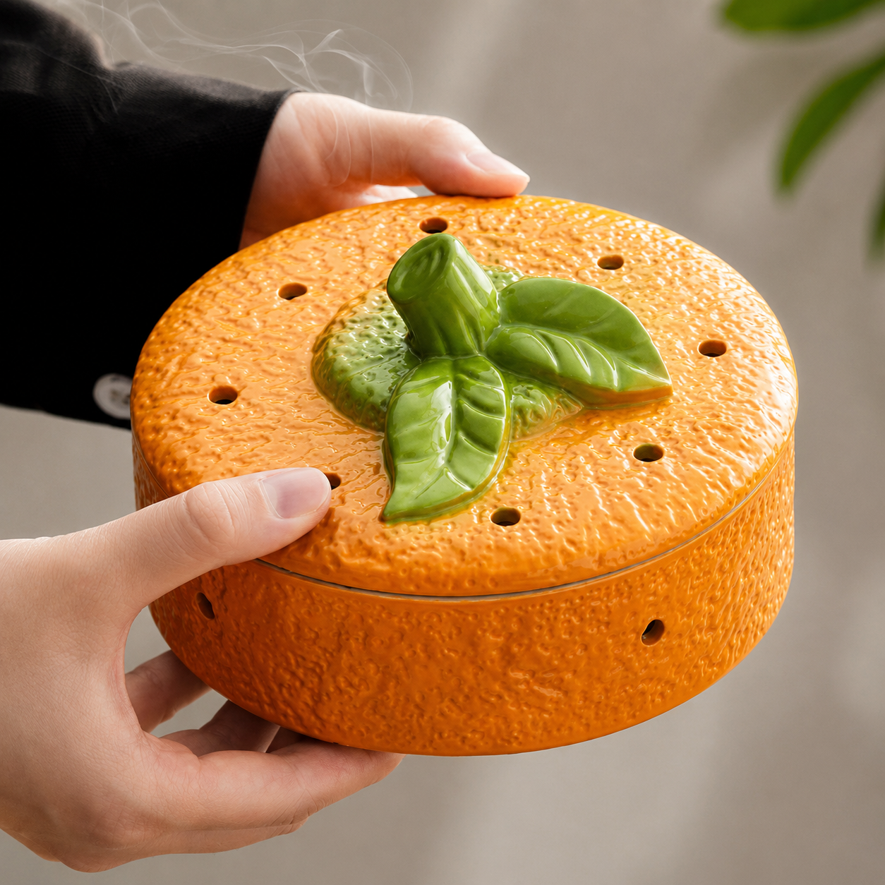 Hand holding persimmon ceramic incense burner showing glossy orange texture and green leaf lid