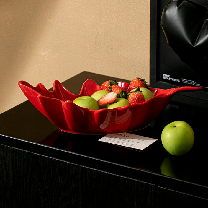 Red ceramic leaf serving bowl styled on dark console table with fruit