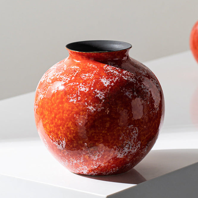 Glossy round orange ceramic vase displayed on white pedestal