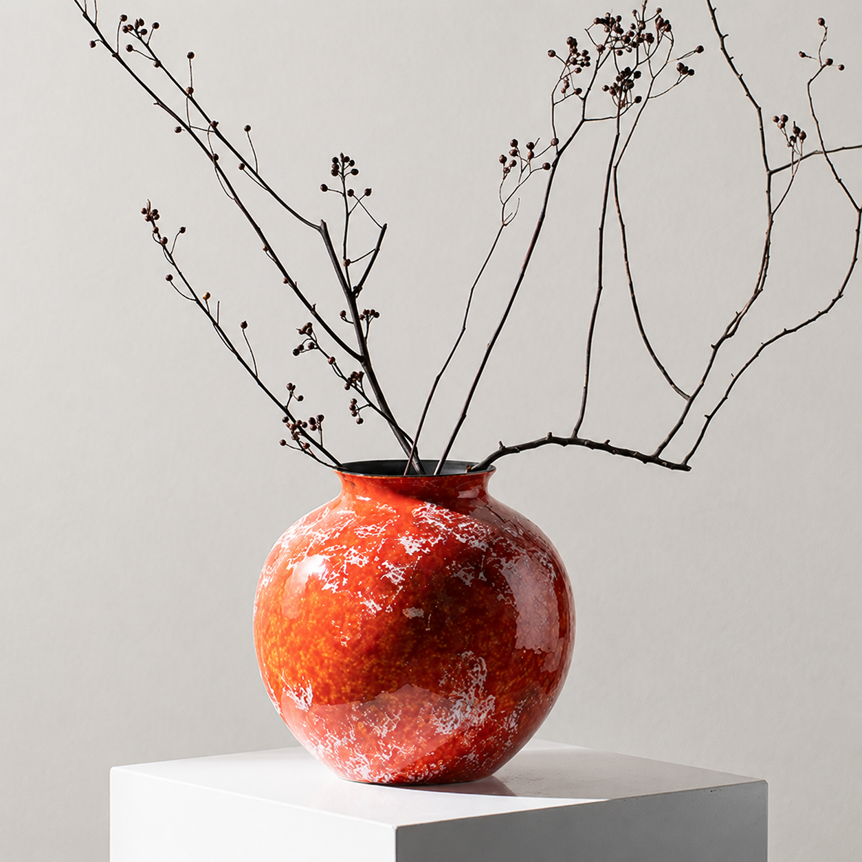 Glossy orange ceramic vase with decorative dried branches on white pedestal