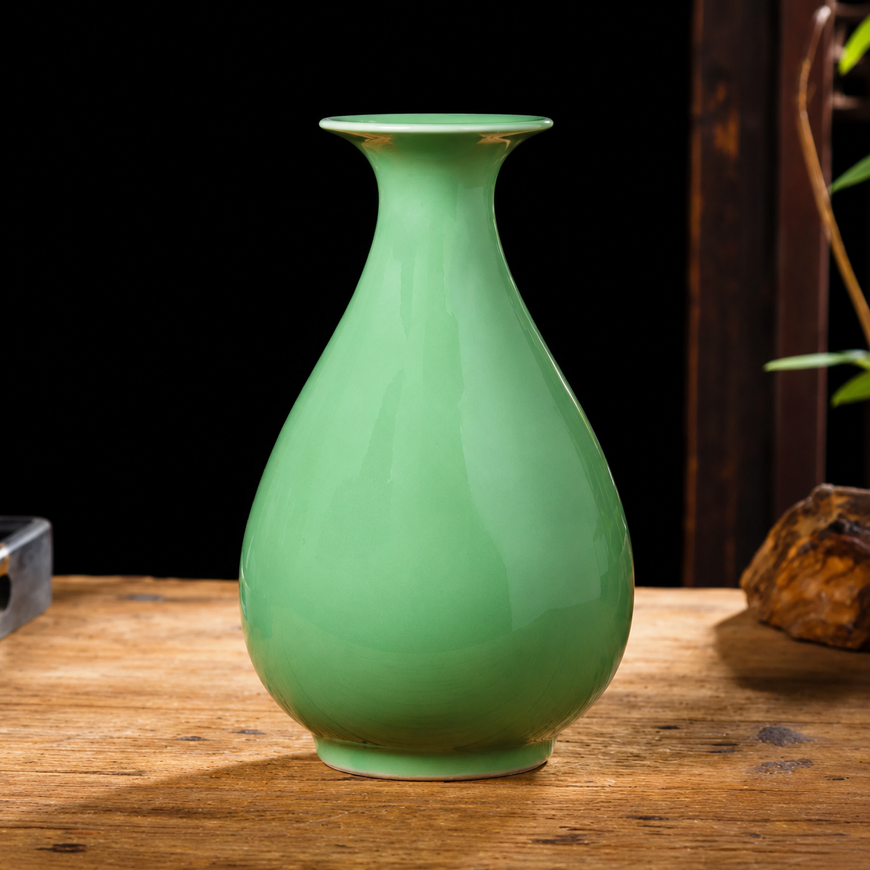 Bulb shaped green ceramic vase with flared rim on wooden table