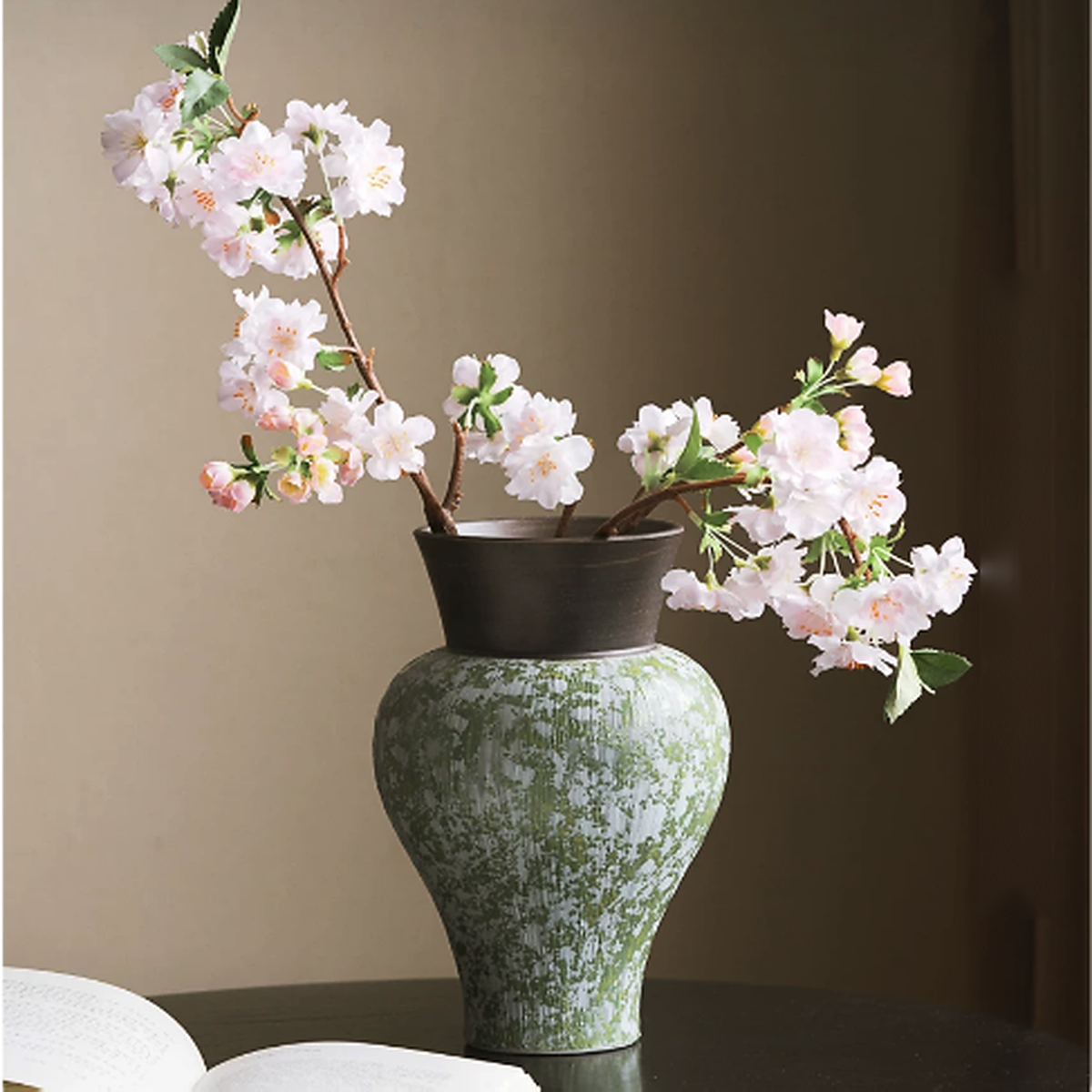 Green speckled ceramic vase with white cherry blossom flowers on table