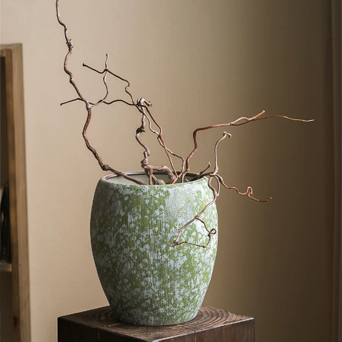 Large green speckled ceramic vase with natural branches on wooden pedestal