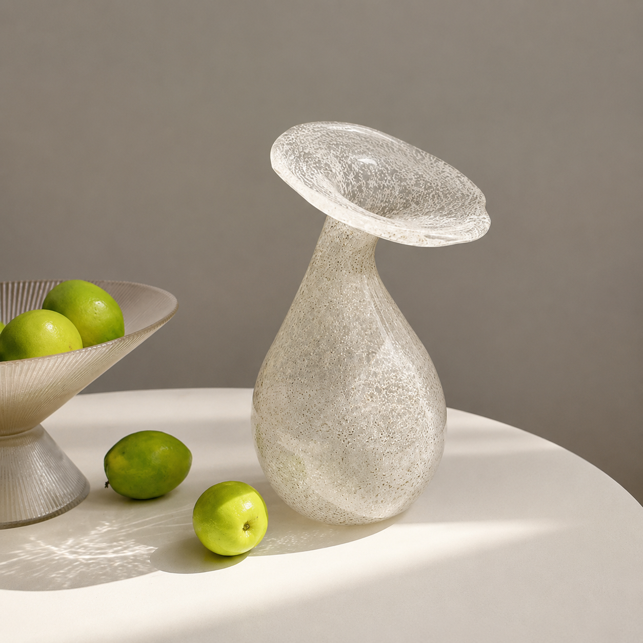Speckled glass bud vase styled with green limes on a soft neutral tabletop