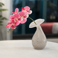 Hand-blown speckled glass bud vase with pink orchid stem on a modern tabletop