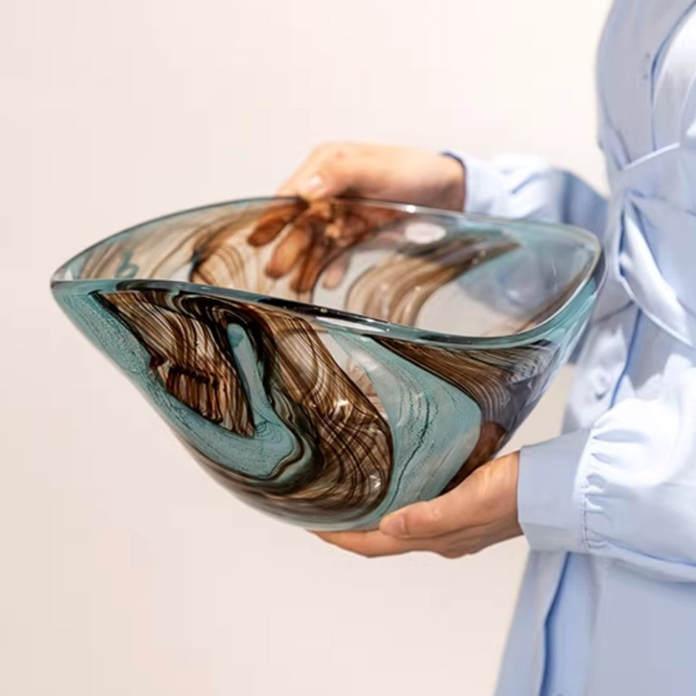 Art glass fruit bowl with flowing blue and brown pattern held in hand to show scale
