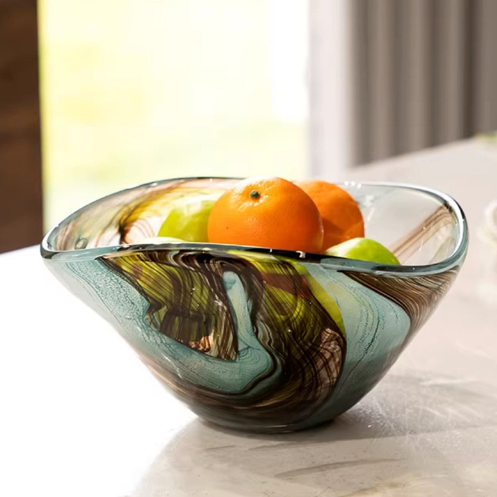 Blue swirl glass fruit bowl with oranges on a marble table near a window
