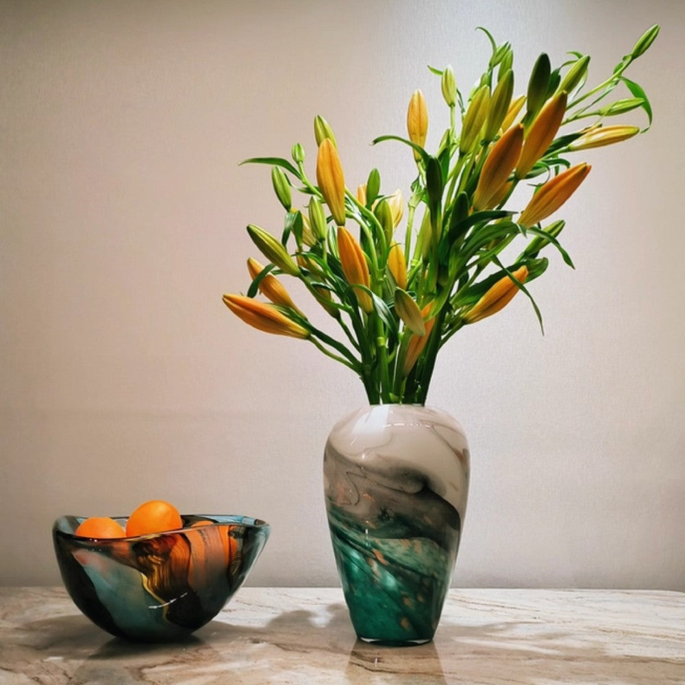 Modern art glass bowl styled beside a matching vase with orange fruit on a console table