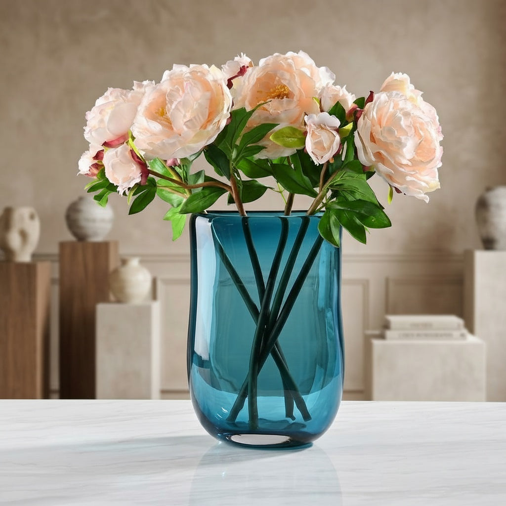 Teal blue glass cylindrical vase styled with pink flowers on a table