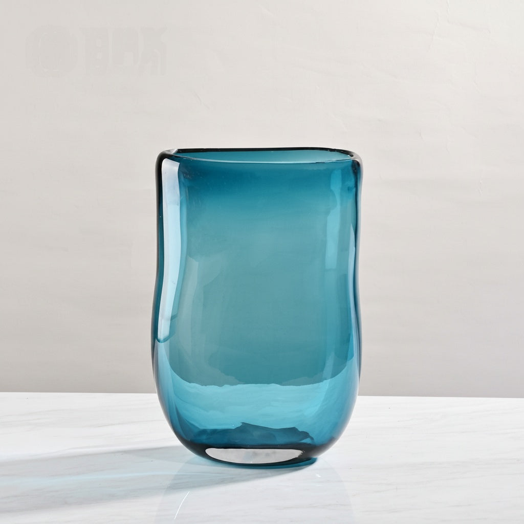 Teal blue glass cylindrical vase on a white marble surface