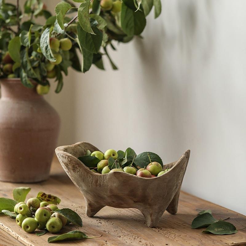 Hand carved wood centerpiece bowl with green fruit beside a potted tree