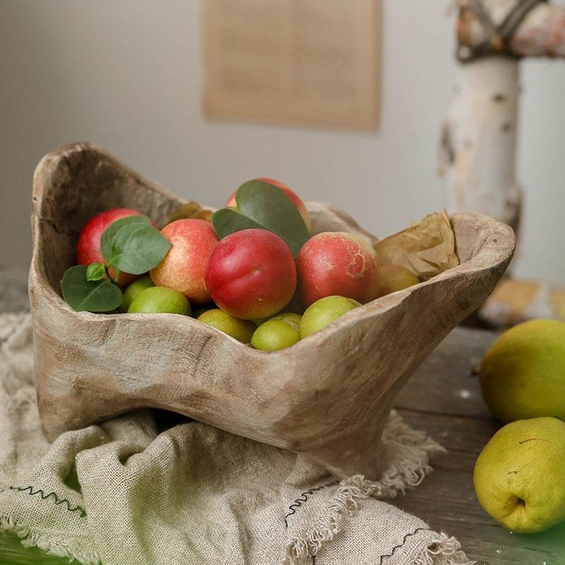 Rustic handmade wood bowl filled with red and green fruit on draped linen