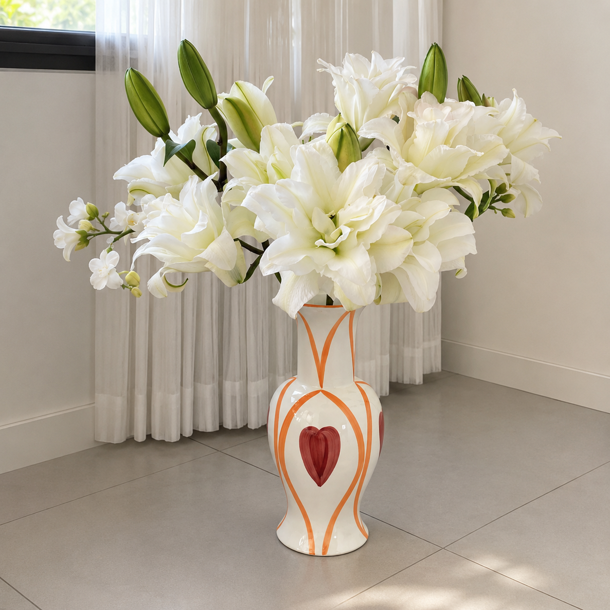 Hand painted ceramic heart vase with white lilies styled by sheer curtains in bright modern interior
