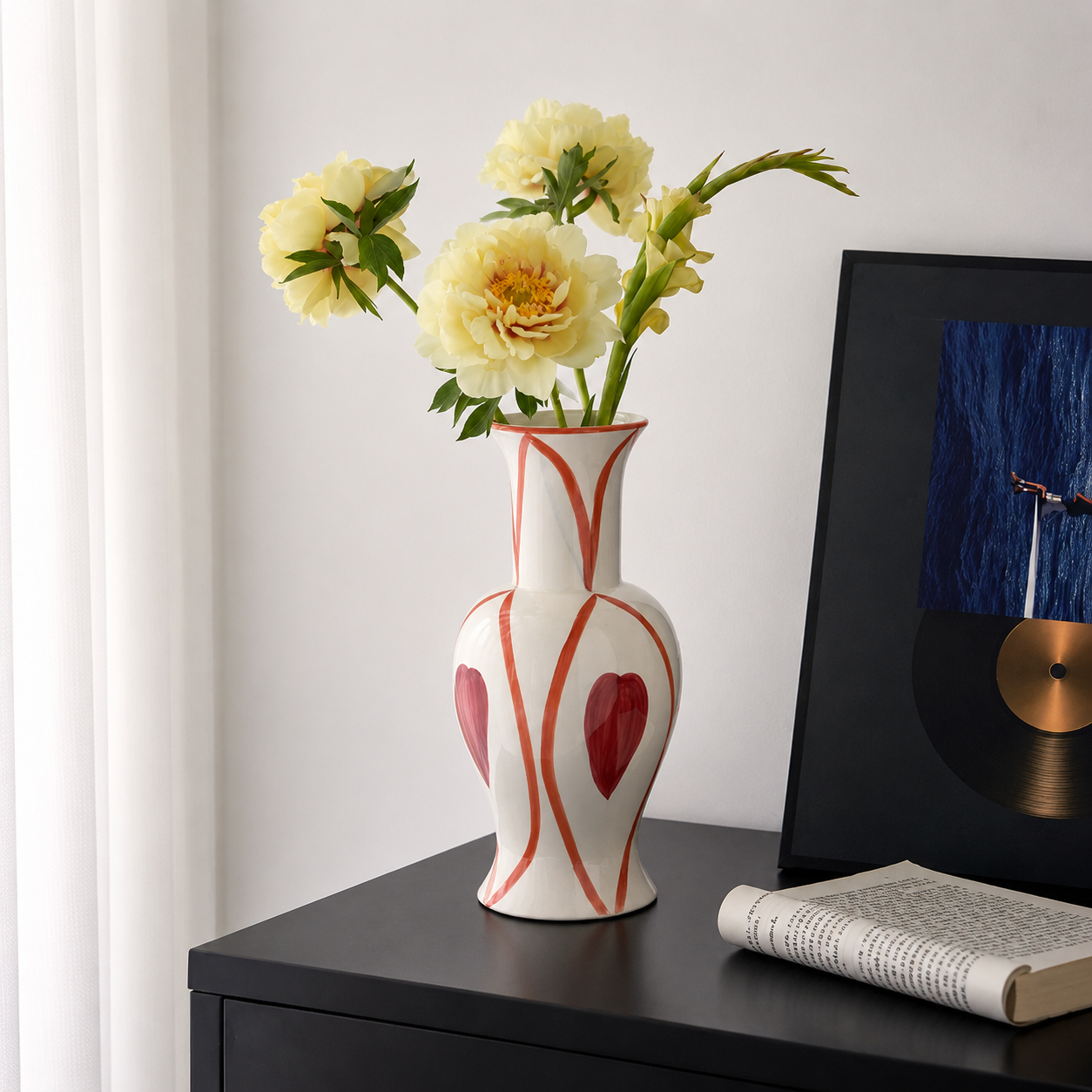 Hand painted heart ceramic flower vase with yellow flowers on black cabinet beside modern wall art