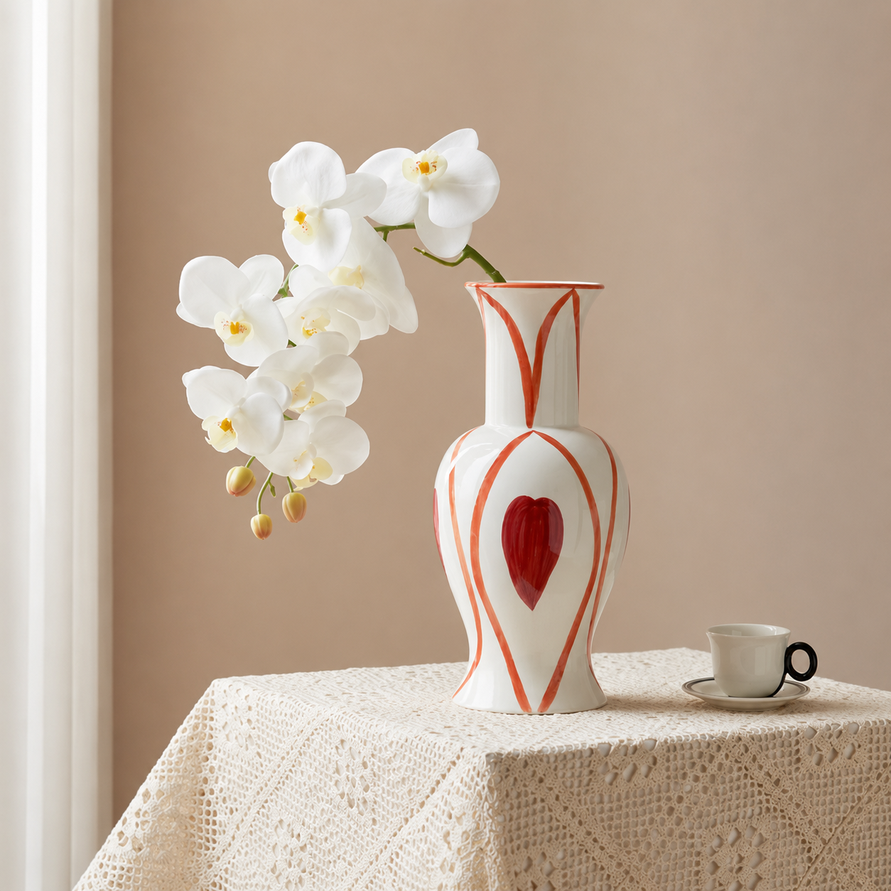 Hand painted heart ceramic vase with white orchids on lace tablecloth beside small coffee cup