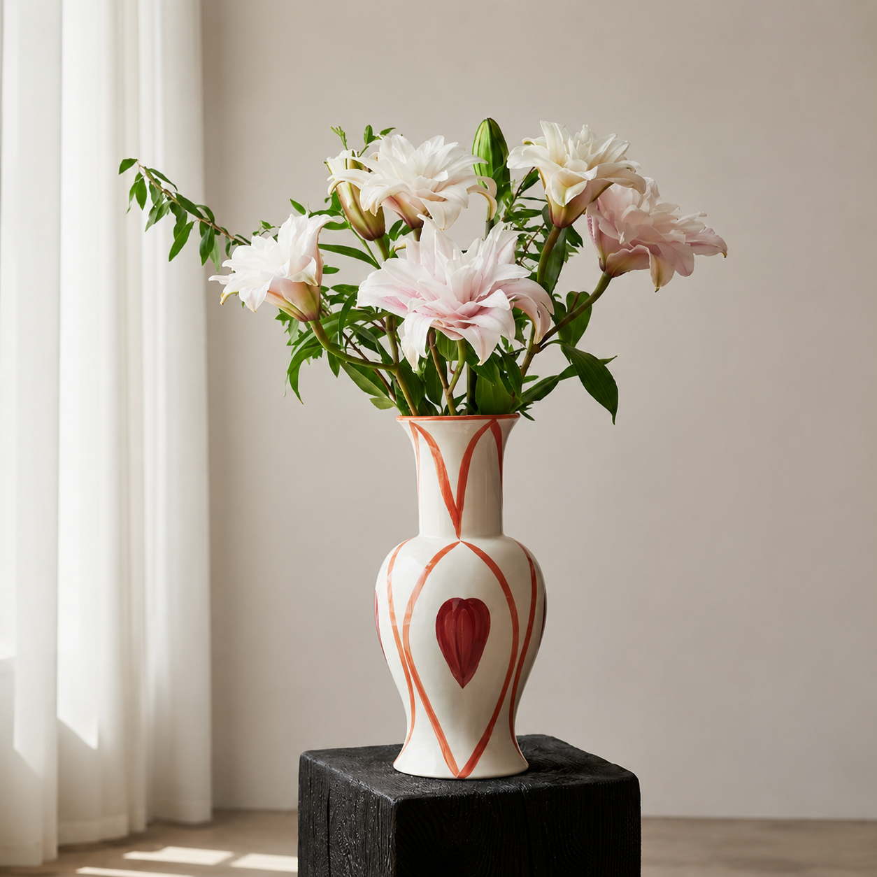Hand painted ceramic heart vase with pale pink flowers displayed on black pedestal near window