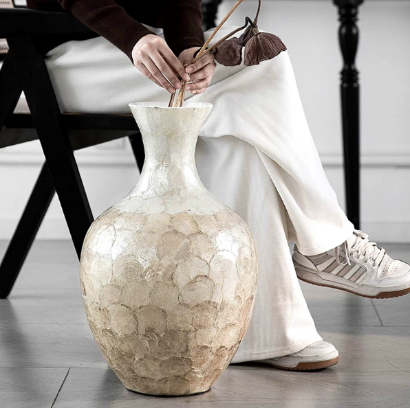 Large handcrafted shell ceramic vase styled beside seated figure for scale
