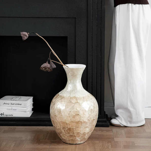 Large shell inlay ceramic vase displayed near black fireplace with dried stems