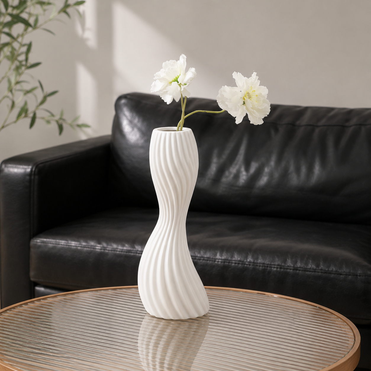 White ribbed ceramic twist vase with white flowers on round coffee table beside black leather sofa