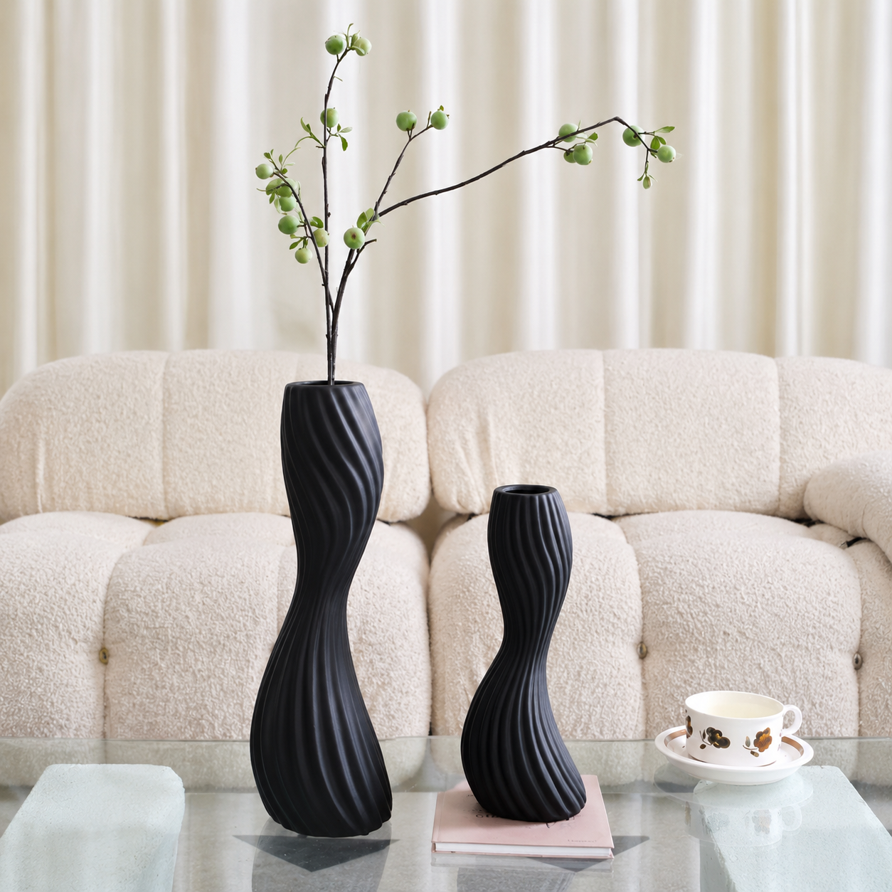 Large and medium black ribbed ceramic twist vases styled on glass coffee table