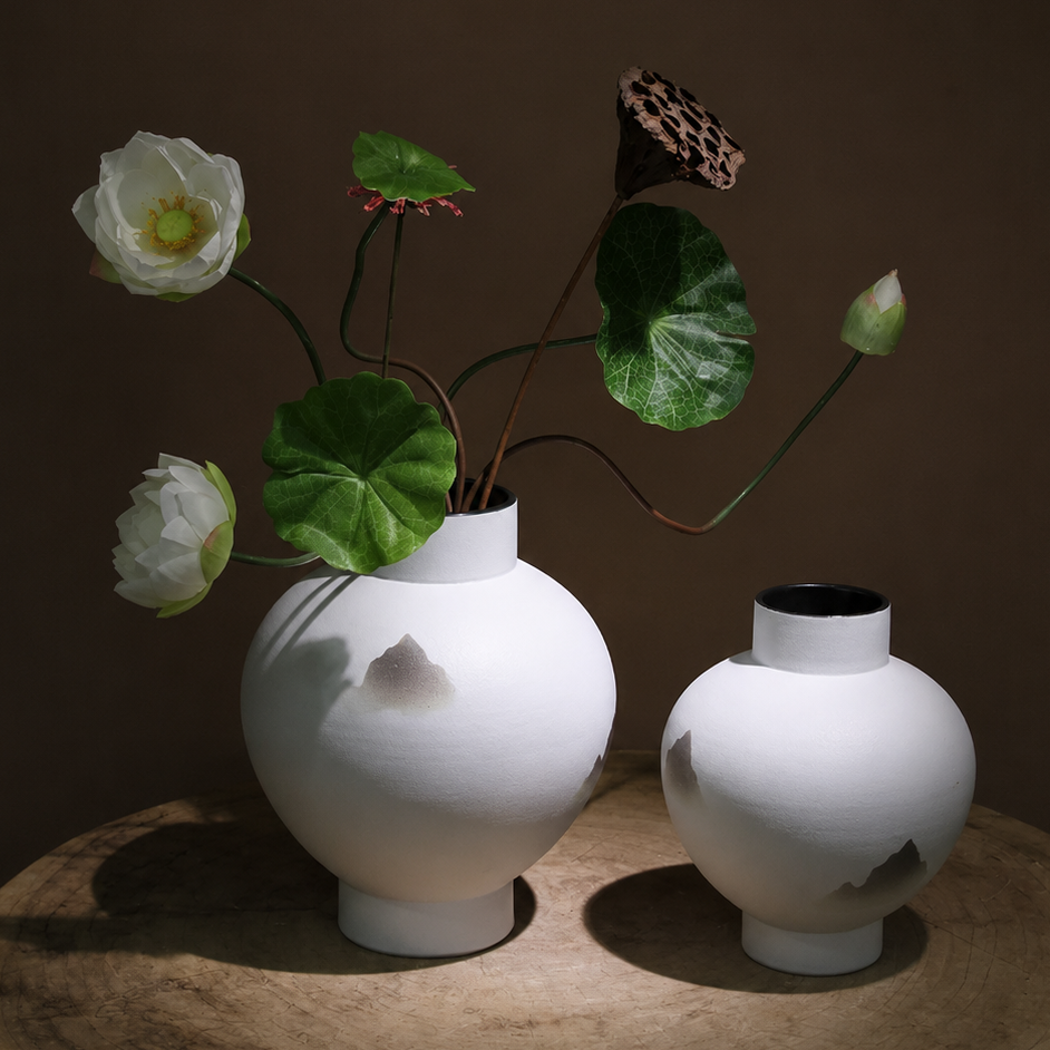 Minimalist ceramic mountain vases with lotus stems on a dark rustic table