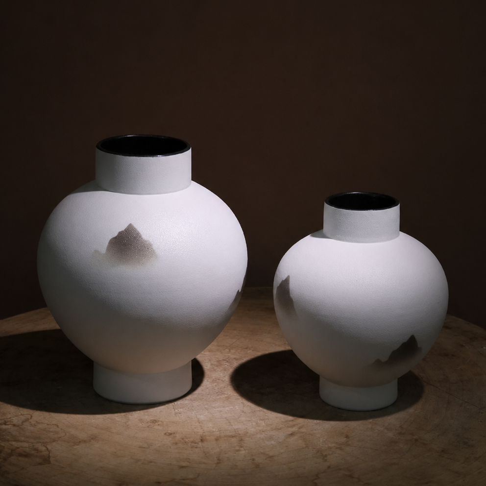 Medium and large white ceramic mountain vases on a dark tabletop