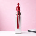 Burgundy sitting abstract figure sculpture on white pedestal against a soft pink background