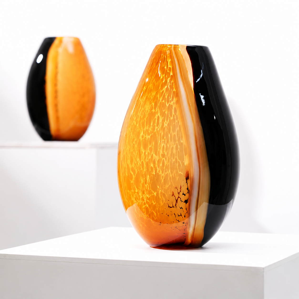 Modern amber and black art glass vase displayed on a white pedestal