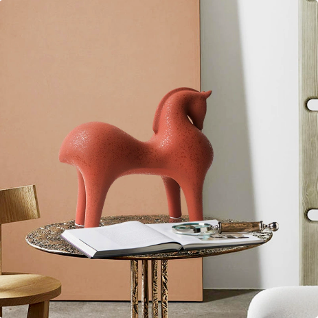 Decorative horse sculpture on a round table with an open book and decorative items against a beige wall.