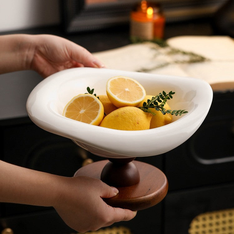 White ceramic pedestal bowl with lemons held above a dark tabletop