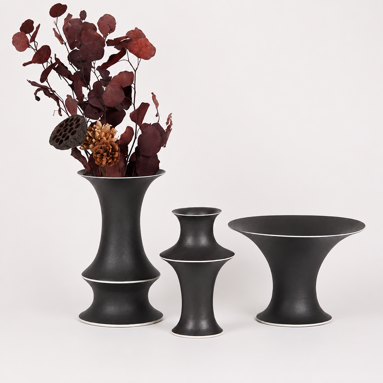 Black ceramic vase trio with dried botanicals and contrast rim on white background