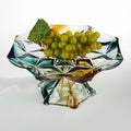 Geometric glass pedestal centerpiece bowl filled with green grapes in teal and amber tones