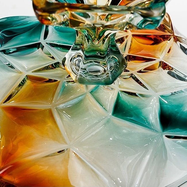 Close up of sculptural faceted glass pedestal base in teal amber and clear tones