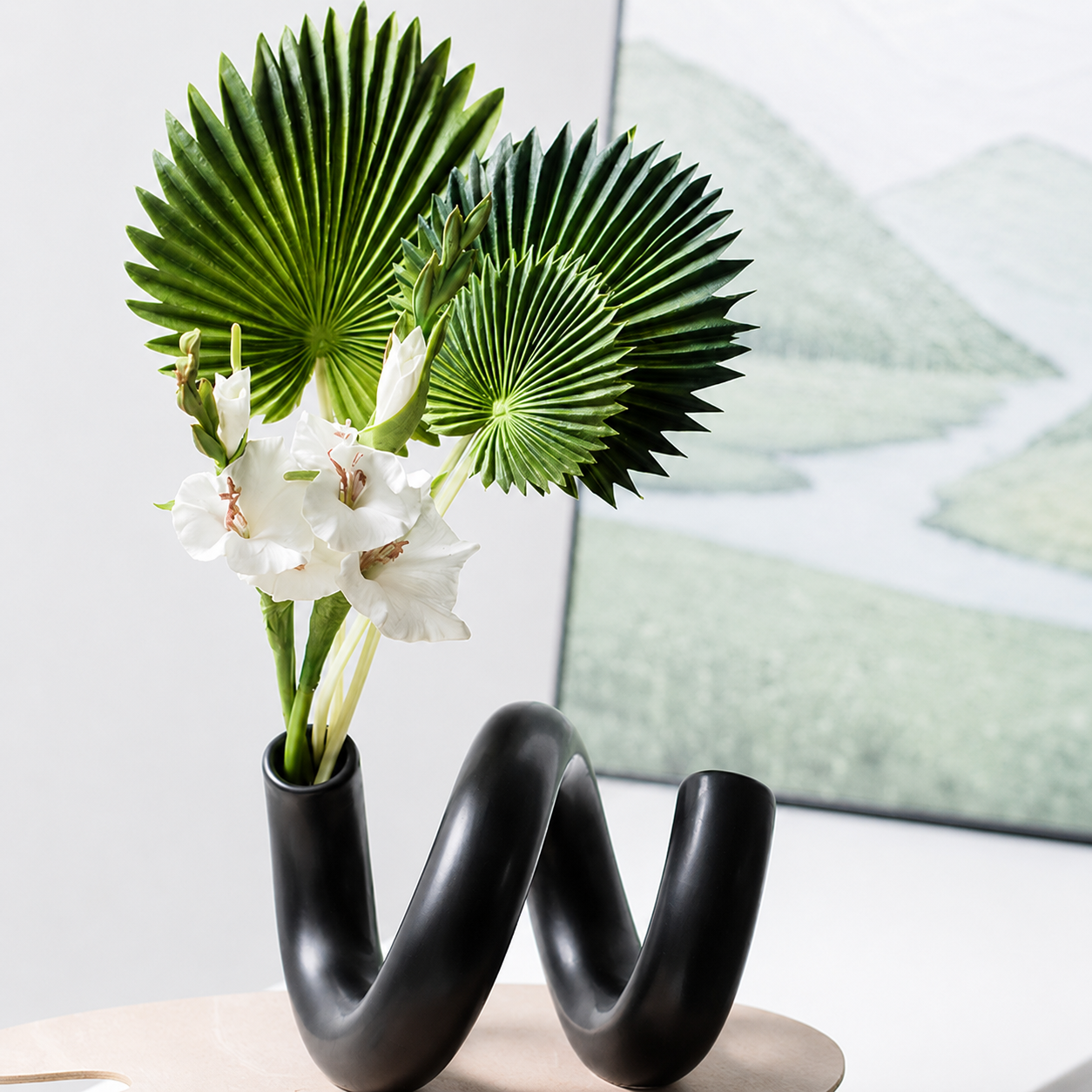 Black loop ceramic vase holding white flowers and green fan palm leaves
