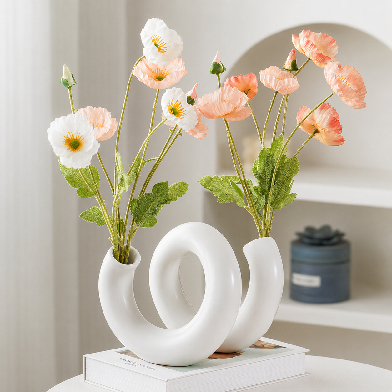 White loop ceramic flower vase styled with peach and white flowers on stacked books