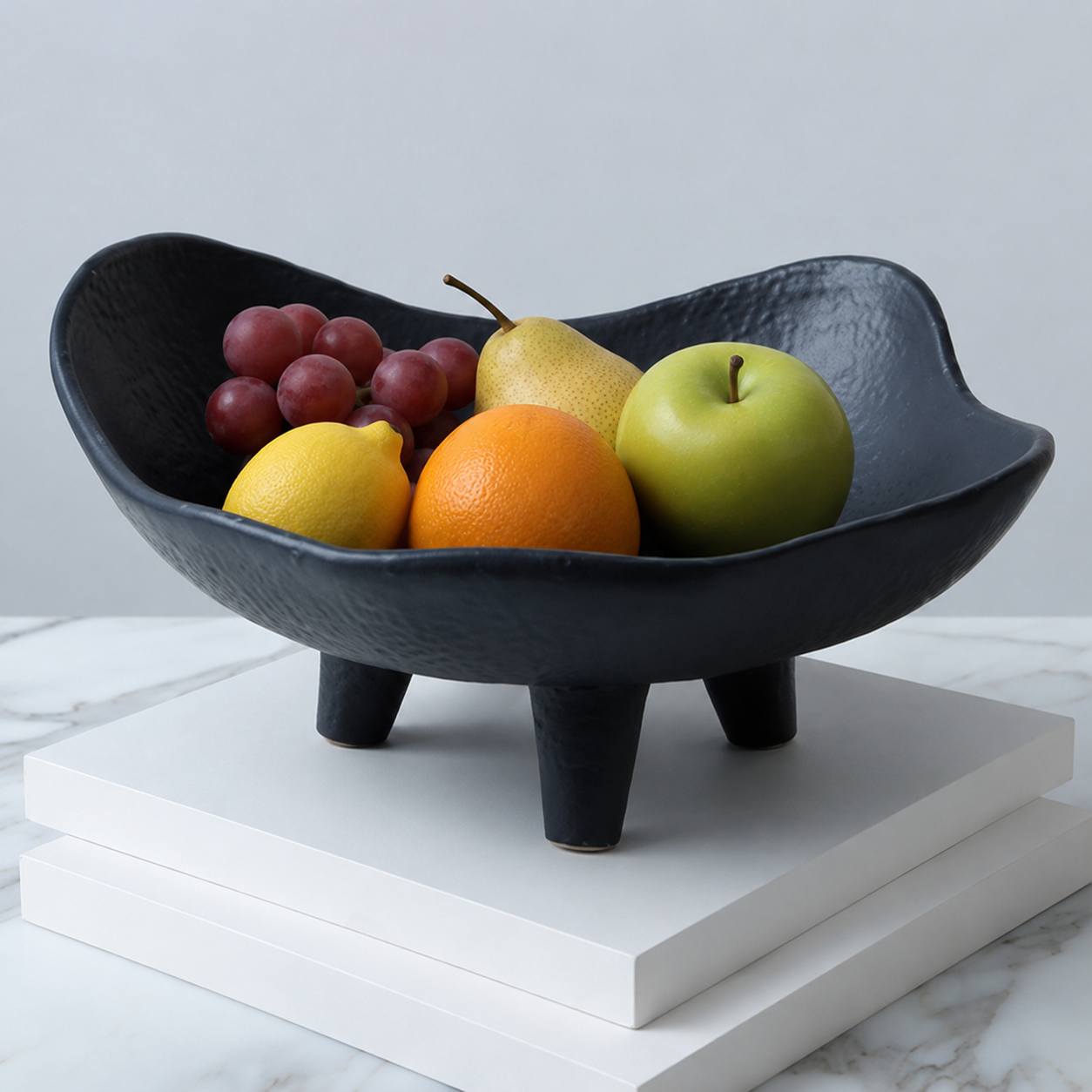 Black modern resin fruit bowl centerpiece styled with mixed fruit on a white display block