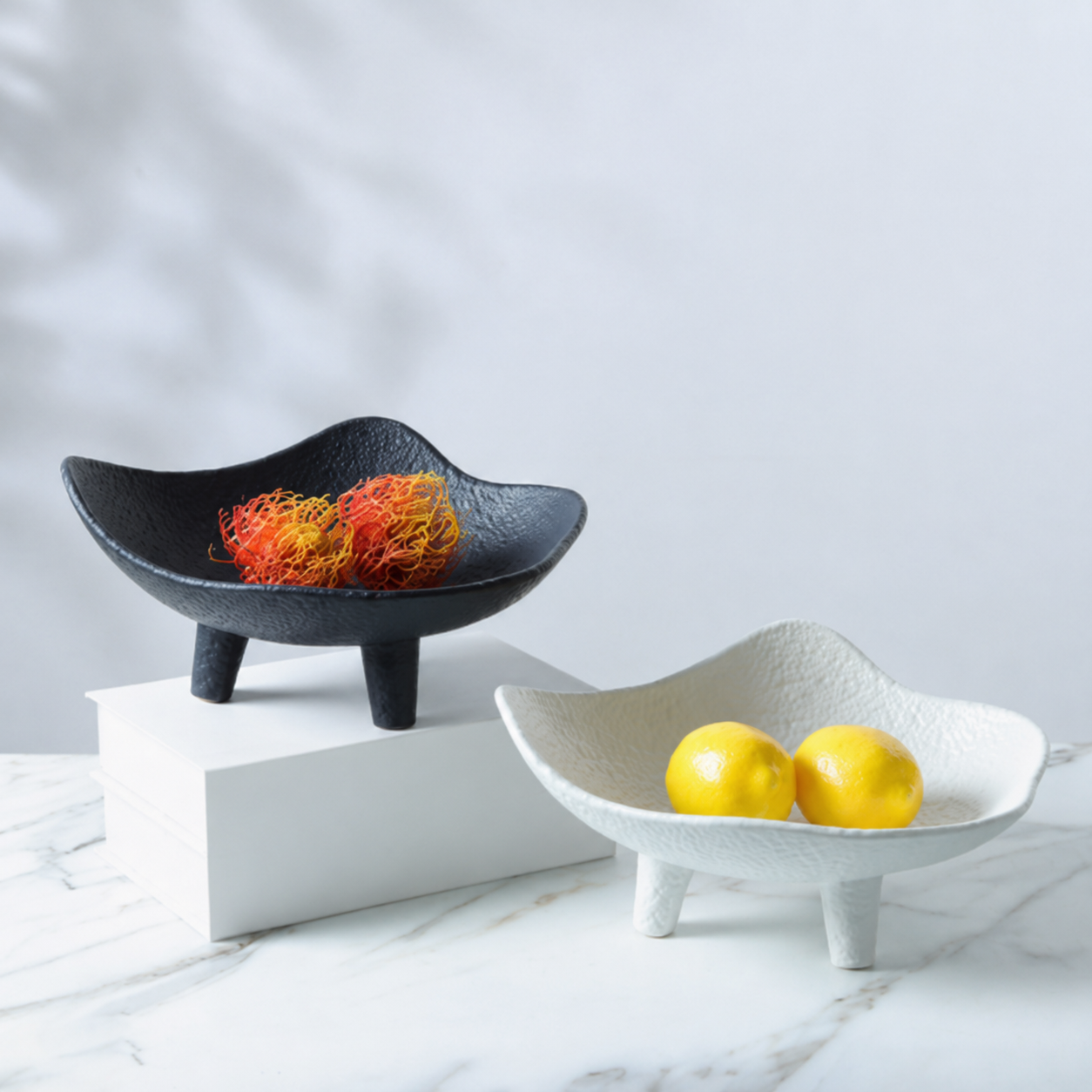 Black and white textured resin footed bowls styled with fruit on a marble surface