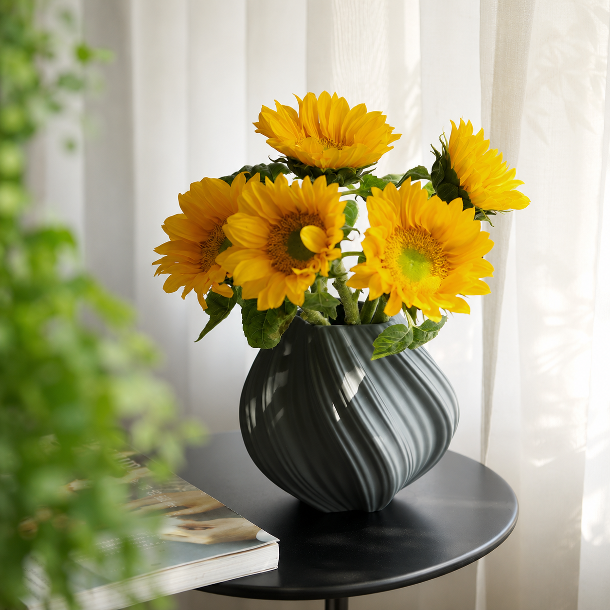 Slate gray ribbed swirl ceramic vase with sunflowers on black side table in bright interior