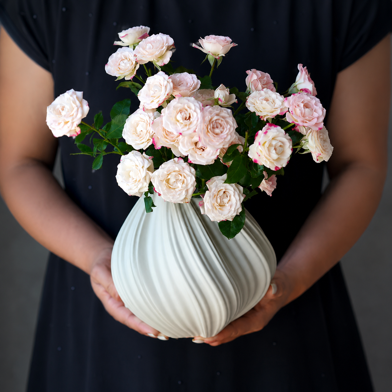 Ivory white ribbed swirl ceramic vase held with pale pink flowers for elegant flower arrangement