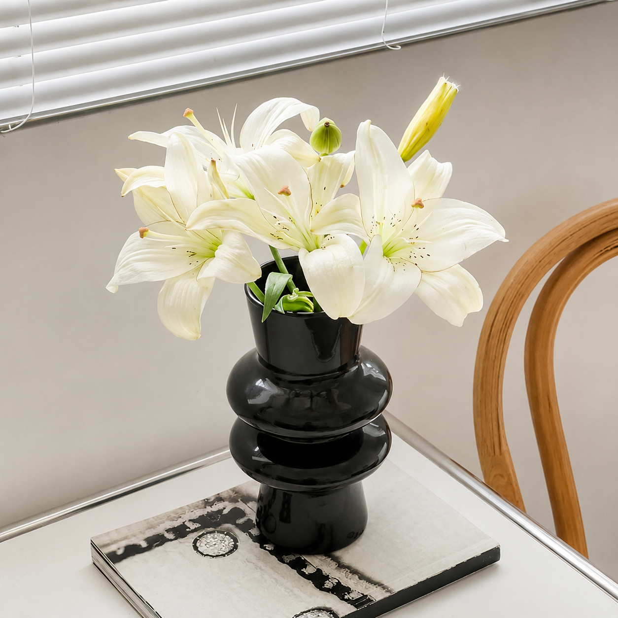 Black sculptural glass vase with white lilies beside a wooden chair