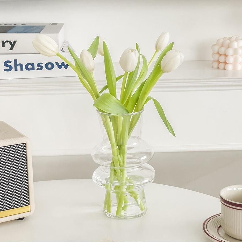 Clear sculptural glass vase holding white tulips on a modern table
